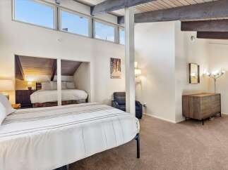 Experience ultimate comfort in this spacious bedroom featuring a vaulted ceiling with exposed beams and large windows that flood the room with natural light.