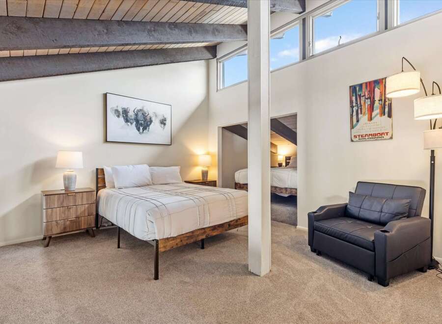 Experience the charm of this unique bedroom featuring a vaulted ceiling with exposed beams and large windows that flood the space with natural light.