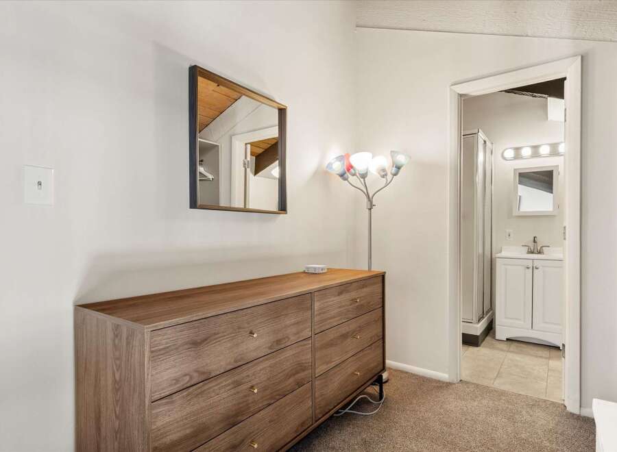 This bedroom features a stylish wooden dresser with brass hardware, complemented by a modern floor lamp and a decorative mirror.
