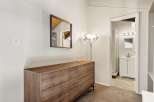 This bedroom features a stylish wooden dresser with brass hardware, complemented by a modern floor lamp and a decorative mirror.