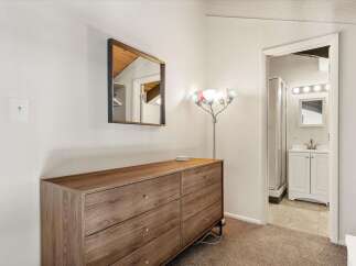 This bedroom features a stylish wooden dresser with brass hardware, complemented by a modern floor lamp and a decorative mirror.