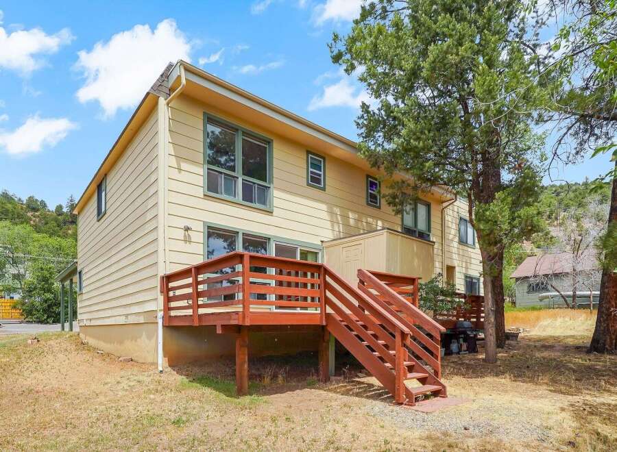Enjoy outdoor living with this charming home featuring a spacious wooden deck and stairs, perfect for entertaining or relaxing amidst a natural setting.