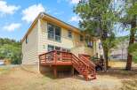 Enjoy outdoor living with this charming home featuring a spacious wooden deck and stairs, perfect for entertaining or relaxing amidst a natural setting.