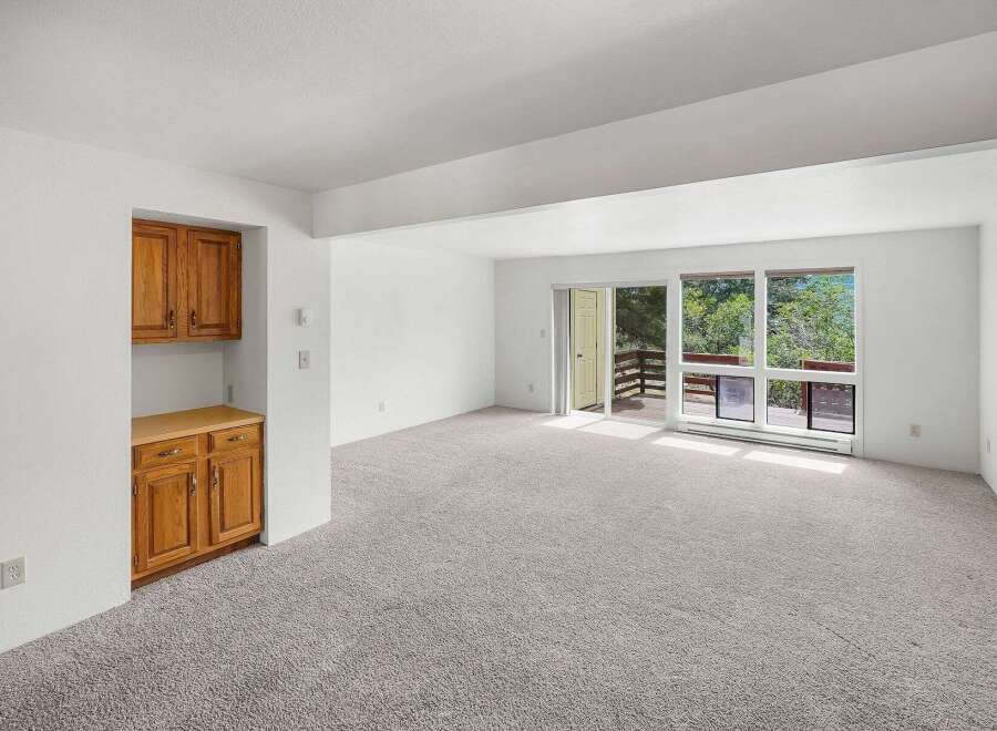 Step into this bright and airy living space, featuring plush carpeting and abundant natural light pouring in through large windows and a sliding glass door.