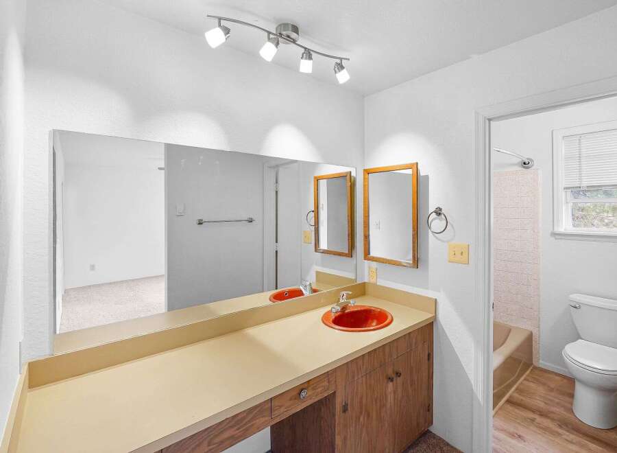 This bathroom features a spacious vanity with a bright orange sink and a large mirror, perfect for getting ready.