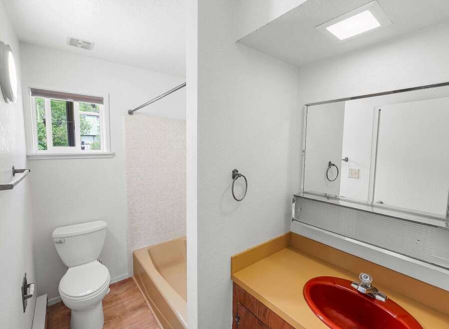 This bathroom features a clean white toilet and a tan bathtub with a textured tile surround.