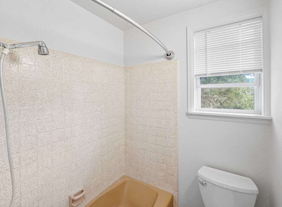 This bathroom features a classic tan bathtub and a tiled shower surround, offering a timeless aesthetic.