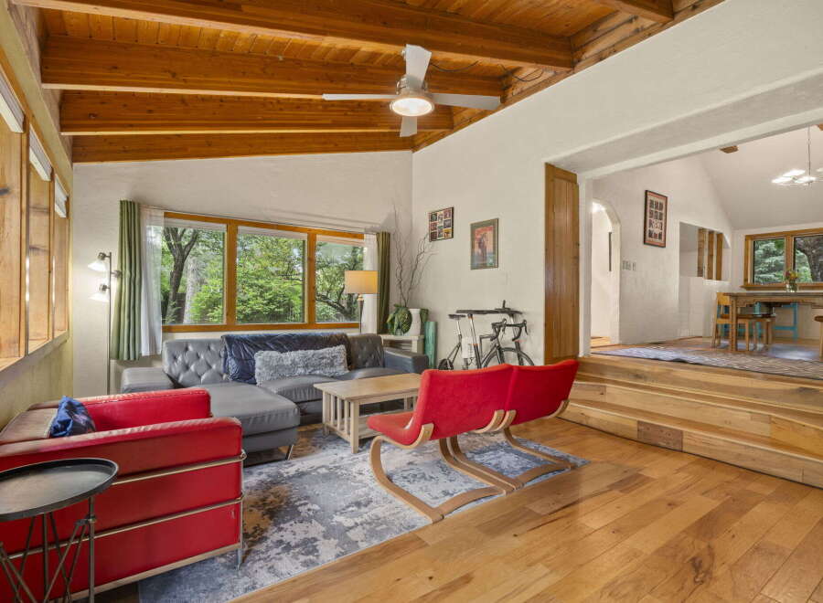 Experience rustic charm in this inviting living space featuring a vaulted wood-beamed ceiling and abundant natural light from large windows.