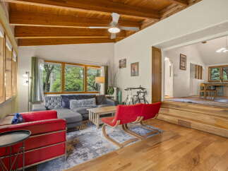 Experience rustic charm in this inviting living space featuring a vaulted wood-beamed ceiling and abundant natural light from large windows.