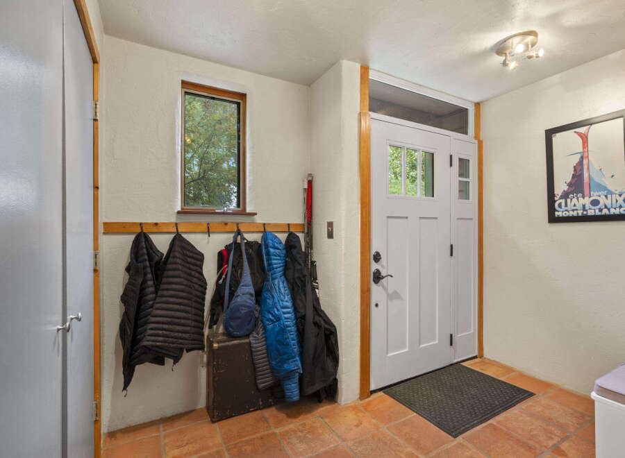 Welcome guests into this charming entryway featuring a wooden coat rack adorned with jackets and a vintage trunk.