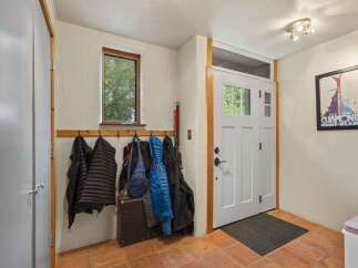 Welcome guests into this charming entryway featuring a wooden coat rack adorned with jackets and a vintage trunk.