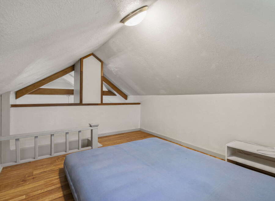 Discover this charming attic bedroom, featuring a cozy blue mattress laid directly on the wooden floor.