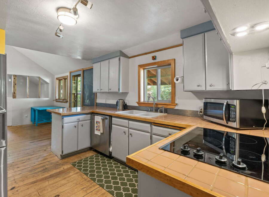 Discover this charming kitchen featuring light gray cabinetry and a tiled backsplash, complemented by a sleek electric stovetop and a built-in microwave.