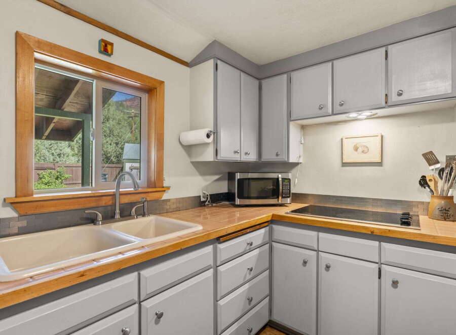 This charming kitchen features a double basin sink with a modern faucet, complemented by a warm wooden countertop and backsplash.