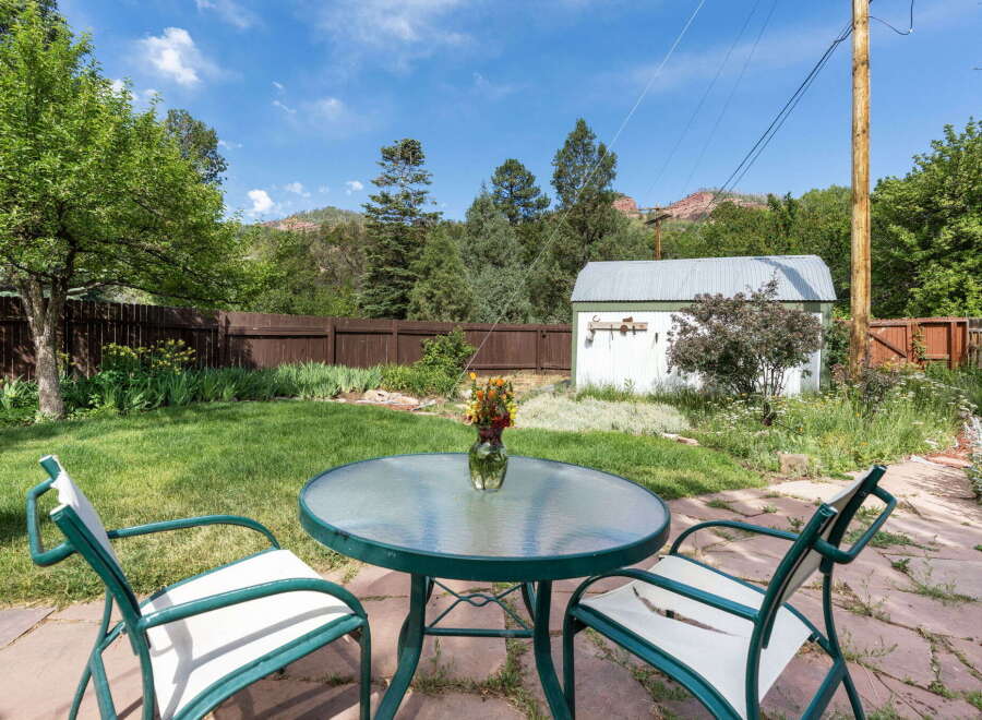 Enjoy outdoor living in this charming backyard featuring a paved patio area with a glass-top table and chairs, perfect for al fresco dining.