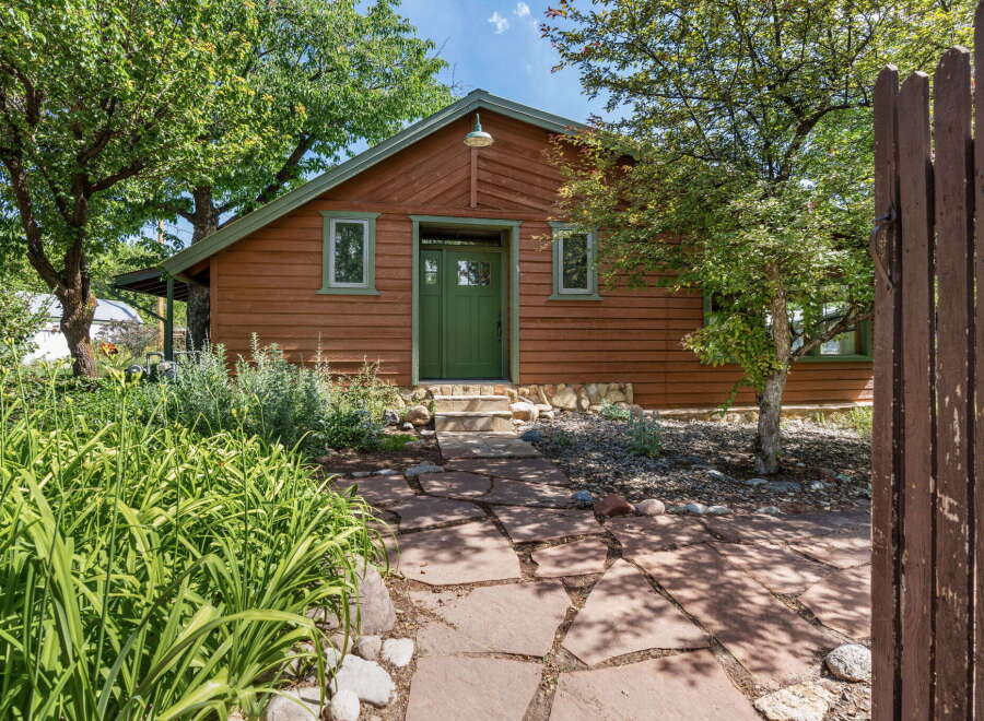 Charming wooden cabin with a vibrant green door and windows, nestled amongst lush trees and mature landscaping.