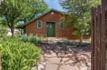 Charming wooden cabin with a vibrant green door and windows, nestled amongst lush trees and mature landscaping.