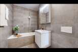This modern bathroom features a sleek white vanity with ample storage, complemented by a spacious bathtub and a rainfall showerhead.