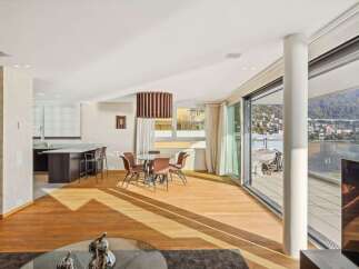 Experience modern living in this spacious open-plan apartment featuring a sleek kitchen island with bar seating, a cozy dining area, and expansive sliding glass doors leading to a balcony with breathtaking water and city views.