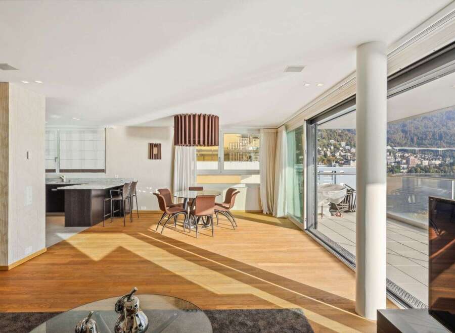 Experience modern living in this spacious open-plan apartment featuring a sleek kitchen island with bar seating, a cozy dining area, and expansive sliding glass doors leading to a balcony with breathtaking water and city views.