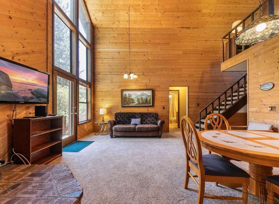 Experience rustic charm in this spacious living area featuring a soaring wood-paneled ceiling and a wall of windows that flood the space with natural light.