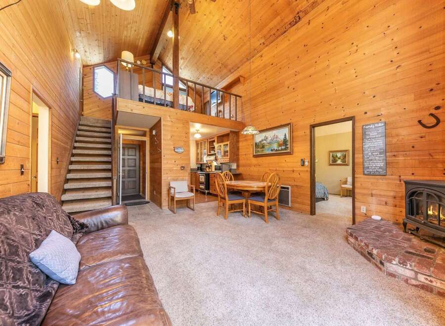 Experience rustic charm in this cozy living space featuring a warm, wood-paneled interior and a prominent brick fireplace with a wood-burning stove.