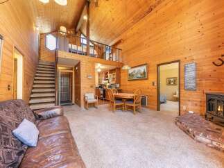 Experience rustic charm in this cozy living space featuring a warm, wood-paneled interior and a prominent brick fireplace with a wood-burning stove.
