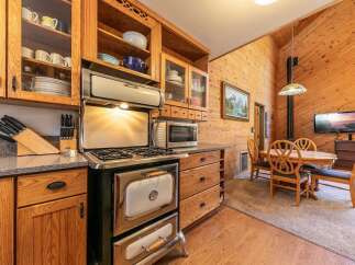 This charming kitchen boasts a vintage-style gas range and oven, complemented by ample wooden cabinetry and glass-front display shelves.