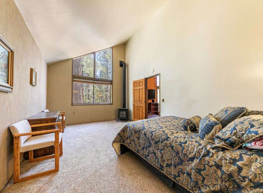 Experience rustic charm in this spacious bedroom featuring a vaulted ceiling and large windows that offer stunning forest views.