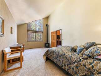 Experience rustic charm in this spacious bedroom featuring a vaulted ceiling and large windows that offer stunning forest views.