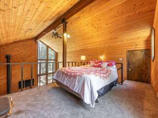 Experience rustic charm in this loft bedroom, featuring a cozy bed with vibrant patterned bedding and a stunning vaulted wood-paneled ceiling.