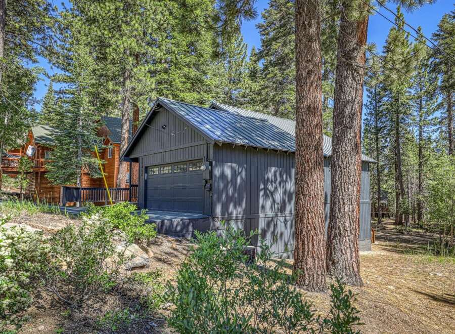 Discover this charming property nestled amongst tall pine trees, featuring a modern dark gray garage with a sleek metal roof.