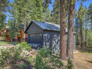 Discover this charming property nestled amongst tall pine trees, featuring a modern dark gray garage with a sleek metal roof.