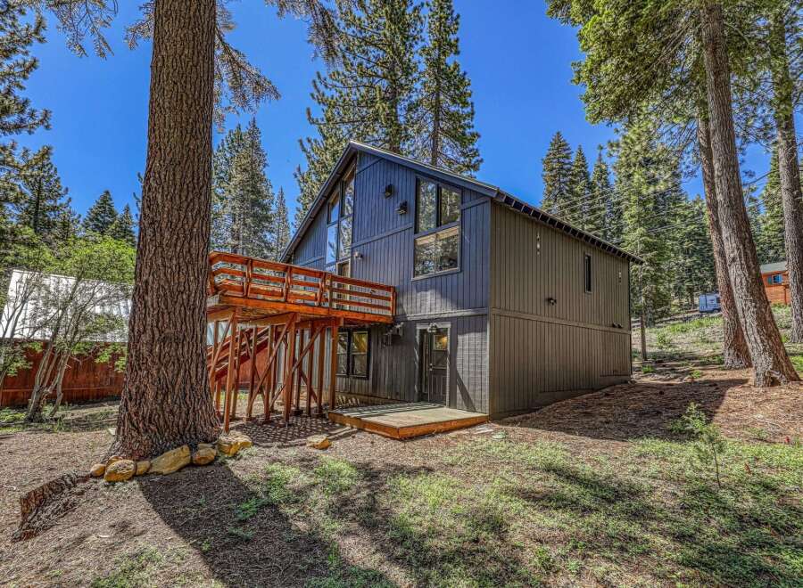 Nestled amongst tall pine trees, this modern mountain home offers a unique architectural design with a striking dark exterior and expansive windows.