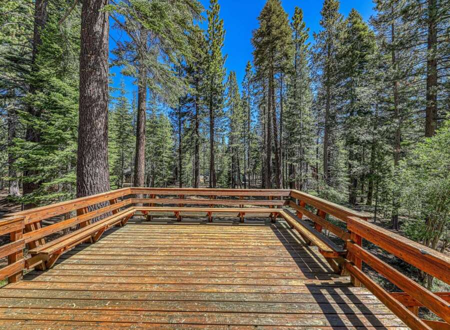 Enjoy the serene mountain lifestyle from this expansive wooden deck, perfect for outdoor gatherings or quiet relaxation amidst towering pine trees.