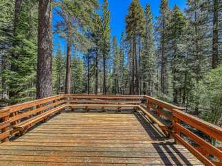 Enjoy the serene mountain lifestyle from this expansive wooden deck, perfect for outdoor gatherings or quiet relaxation amidst towering pine trees.