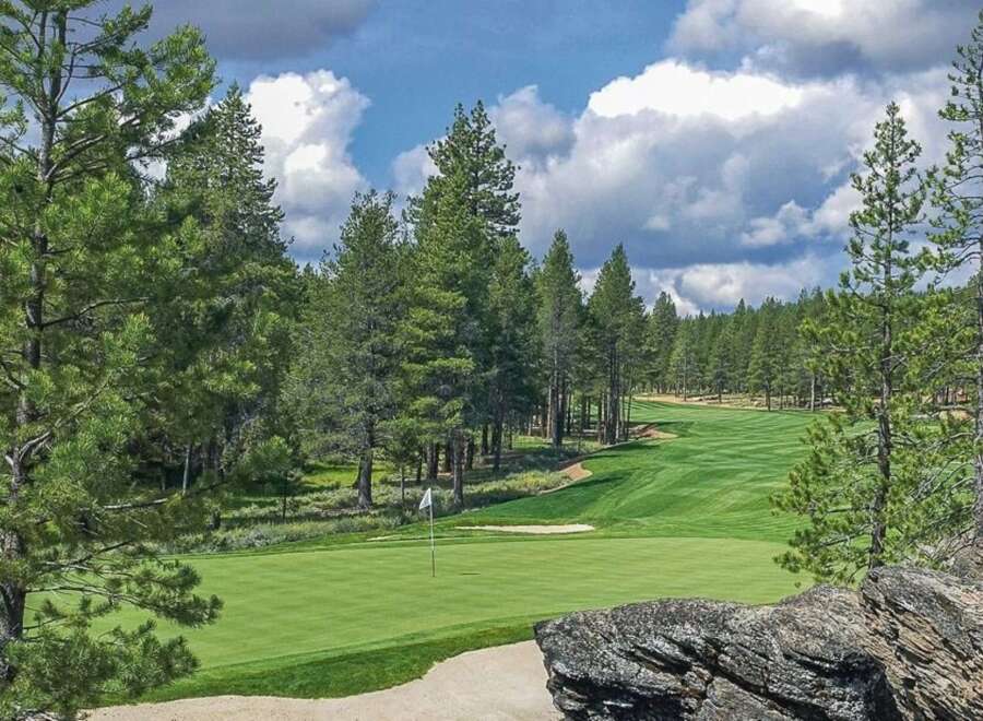 Experience the ultimate golf getaway with this stunning view of a meticulously maintained golf course nestled amongst tall pine trees.