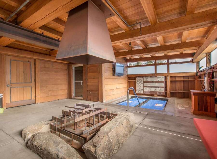 Experience ultimate relaxation in this unique indoor/outdoor spa area, featuring a covered hot tub with a protective blue cover and a modern metal fire pit structure.