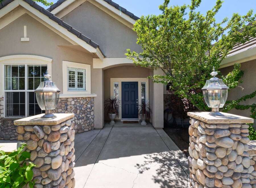 Welcome guests to this charming home with a striking stone-accented entrance, featuring elegant lamp posts and a welcoming dark blue front door.