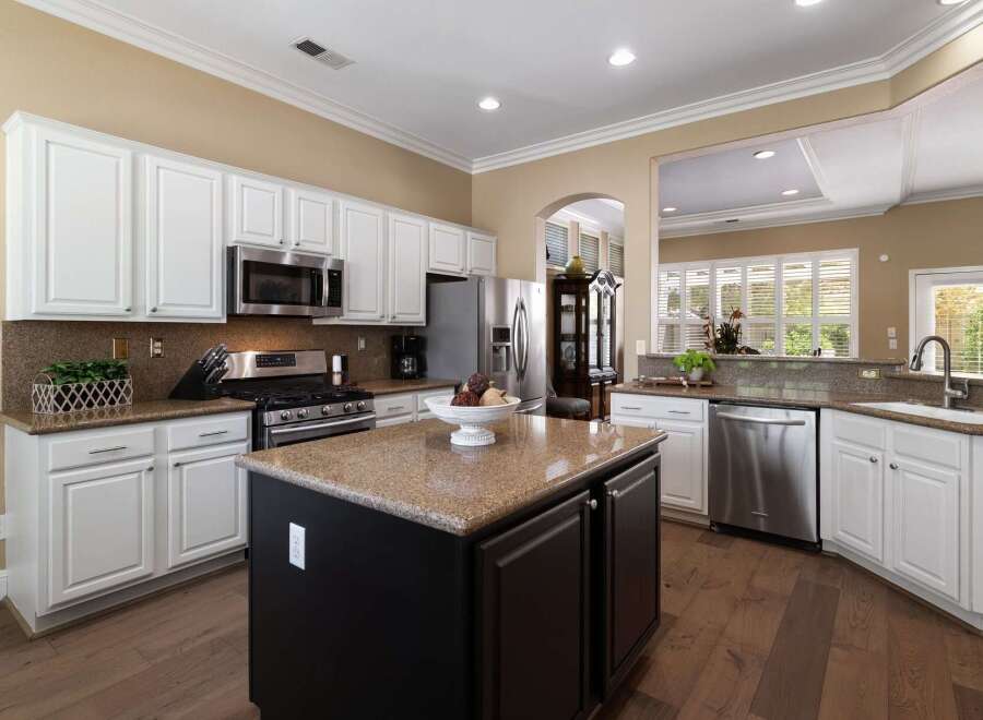 This spacious kitchen features white cabinetry, granite countertops, and a large island with a dark wood base.