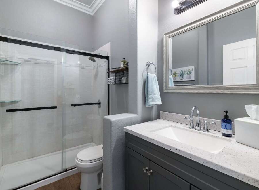 This modern bathroom features a sleek glass-enclosed shower with white tiled walls and black fixtures, complemented by a floating glass shelf.
