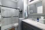 This modern bathroom features a sleek glass-enclosed shower with white tiled walls and black fixtures, complemented by a floating glass shelf.