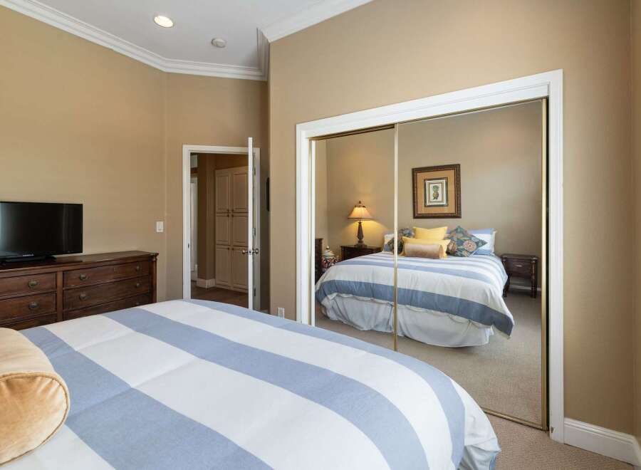 This bedroom features a large dresser with a television and a comfortable bed with blue and white striped bedding.