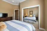This bedroom features a large dresser with a television and a comfortable bed with blue and white striped bedding.
