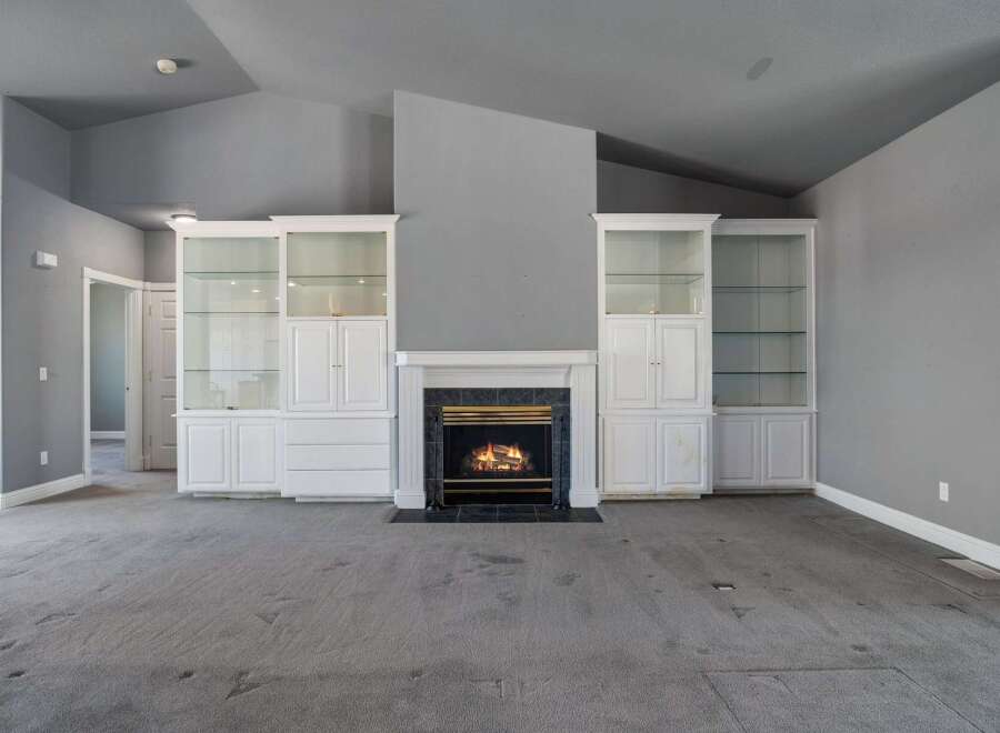 This spacious living room features a cozy fireplace as the focal point, flanked by elegant white built-in display cabinets with glass doors.
