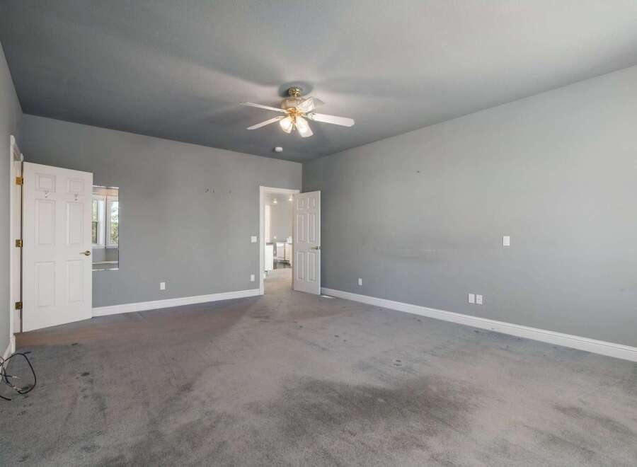 Discover this spacious bedroom featuring a neutral gray palette and a convenient ceiling fan for year-round comfort.