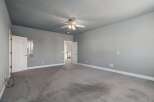 Discover this spacious bedroom featuring a neutral gray palette and a convenient ceiling fan for year-round comfort.