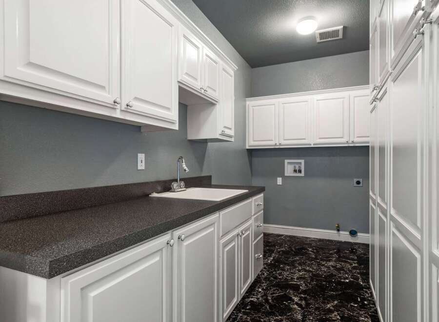 This laundry room boasts ample storage with a combination of upper and lower white cabinets, perfect for organizing supplies.