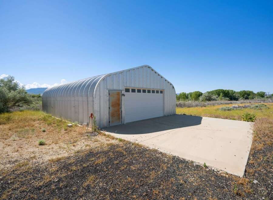 Discover this versatile Quonset hut, perfect for storage or a workshop, featuring a large roll-up garage door and a separate entry door.