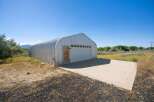Discover this versatile Quonset hut, perfect for storage or a workshop, featuring a large roll-up garage door and a separate entry door.